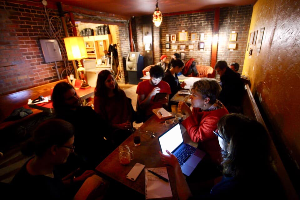 Groupe de membres du Café des savoirs libres discutant de libre-échange marchand et de restriction du droit d'accès culturel dans un bar sombre, le visage éclairé par leurs écrans d'ordinateurs, le 13 octobre dernier.